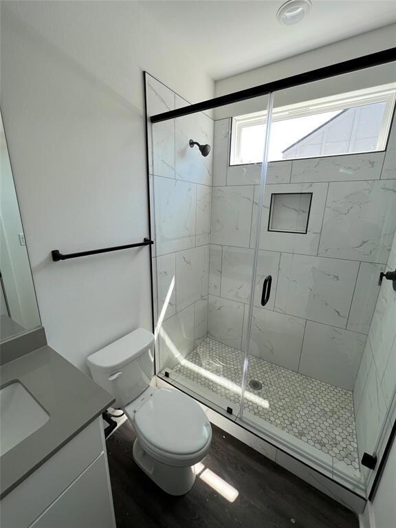 Bathroom featuring toilet, a stall shower, wood f