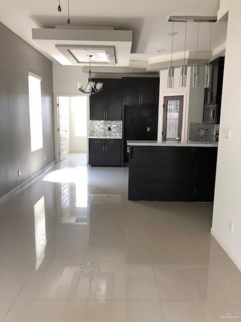 Kitchen featuring dark cabinets, light countertops, a raised ceiling, decorative light fixtures, and tasteful backsplash