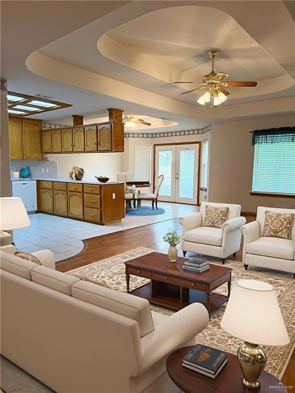 Living room with a tray ceiling, ceiling fan, healthy amount of natural light, and light wood-type flooring