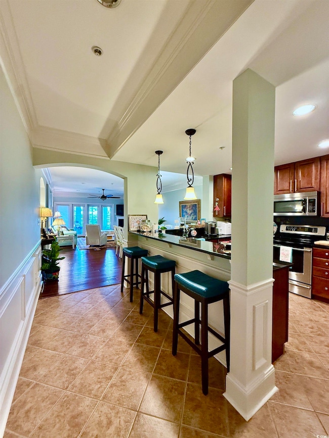 Kitchen with appliances with stainless steel finishes, crown molding, a kitchen breakfast bar, light tile patterned floors, and a ceiling fan