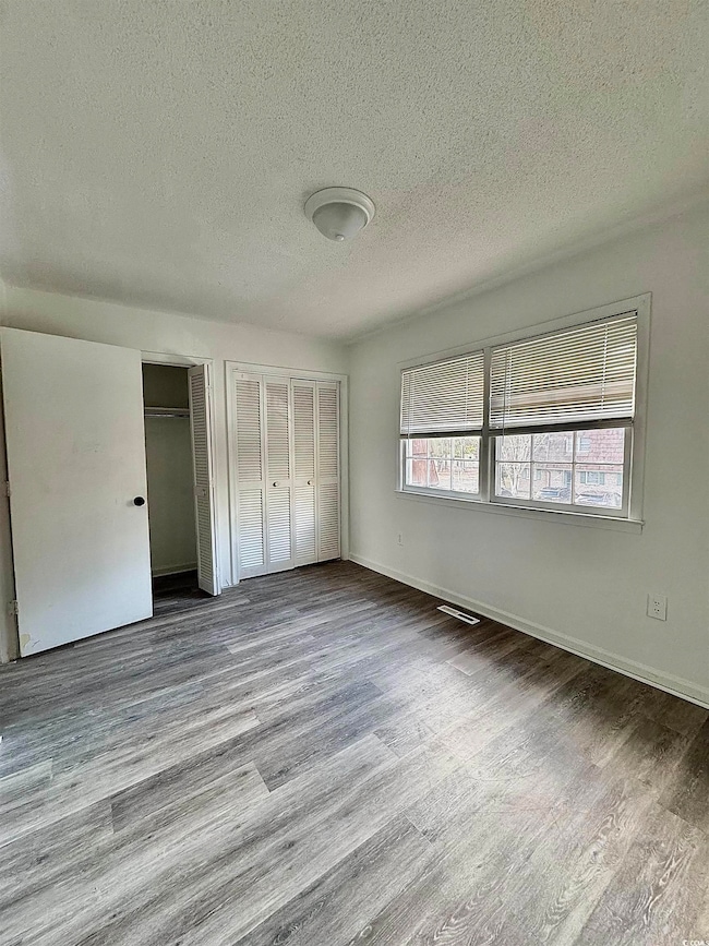 Unfurnished bedroom with two closets, a textured ceiling, and wood finished floors