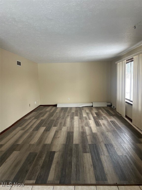 Empty room with dark wood-type flooring and a textured ceiling