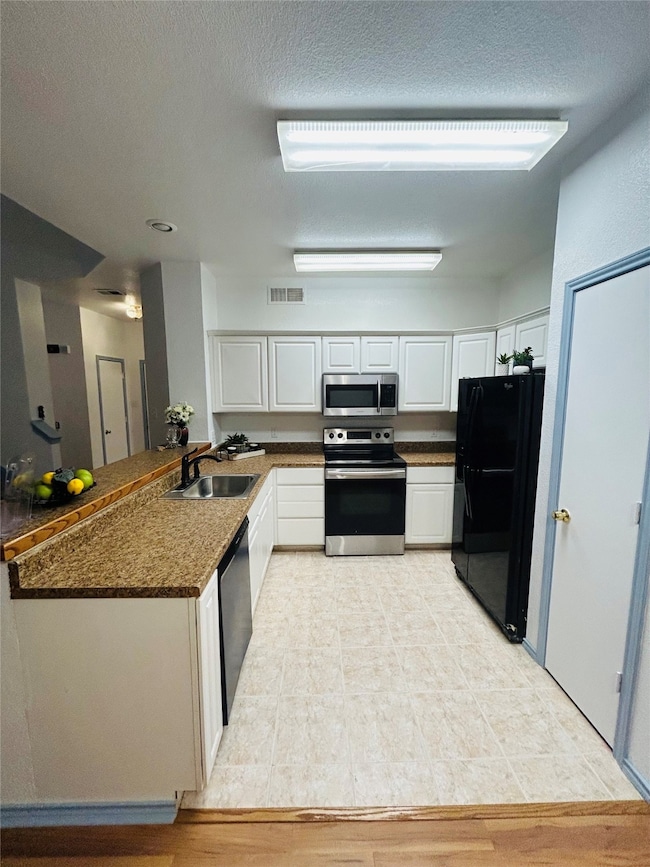 Kitchen featuring appliances with stainless steel finishes, white cabinetry, a textured ceiling, and a peninsula