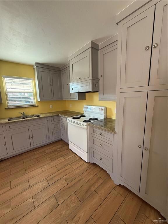 Kitchen with white electric stove, a sink, wood finish floors, extractor fan, and gray cabinetry