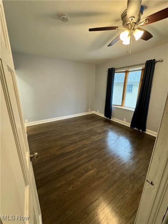 Empty room featuring dark wood-type flooring and ceiling fan