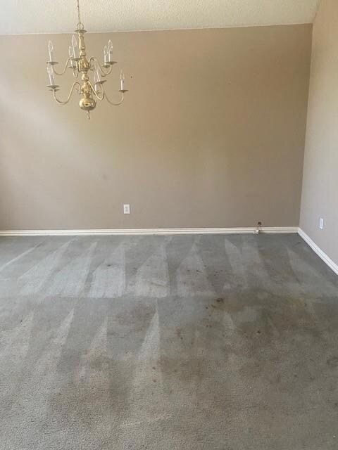 Carpeted empty room with a textured ceiling and an inviting chandelier