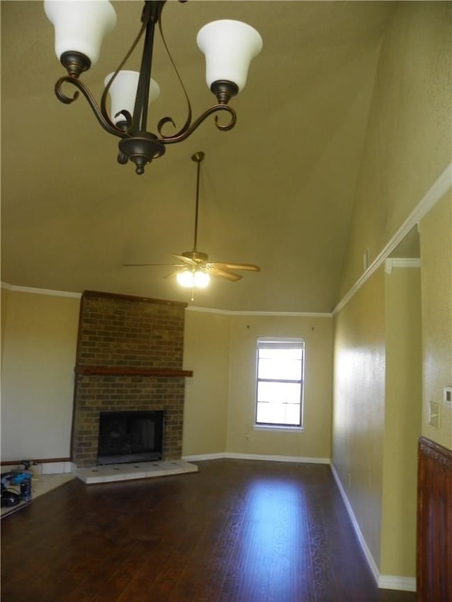 Unfurnished living room featuring a brick fireplace, dark wood-style floors, high vaulted ceiling, a ceiling fan, and a chandelier