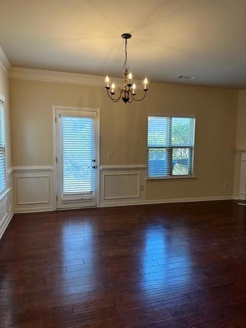Unfurnished dining area featuring a chandelier, healthy amount of natural light, ornamental molding, dark wood-type flooring, and a decorative wall
