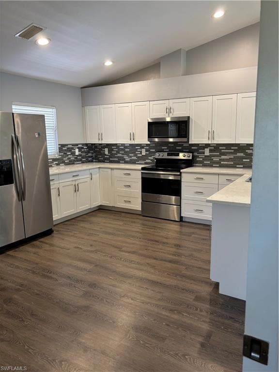 Kitchen with range, refrigerator, white cabinets, backsplash, and vaulted ceiling