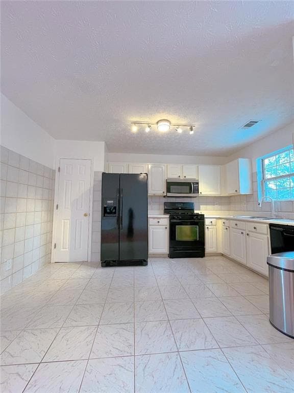 Kitchen with black appliances, light countertops, light marble finish flooring, white cabinetry, and a textured ceiling