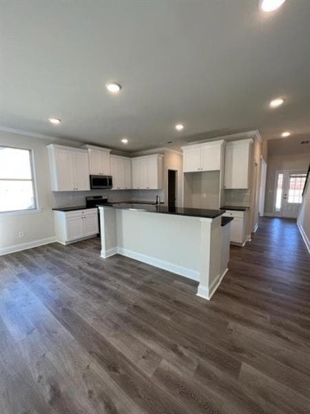 Kitchen featuring stainless steel microwave, dark countertops, baseboards, recessed lighting, and white cabinetry