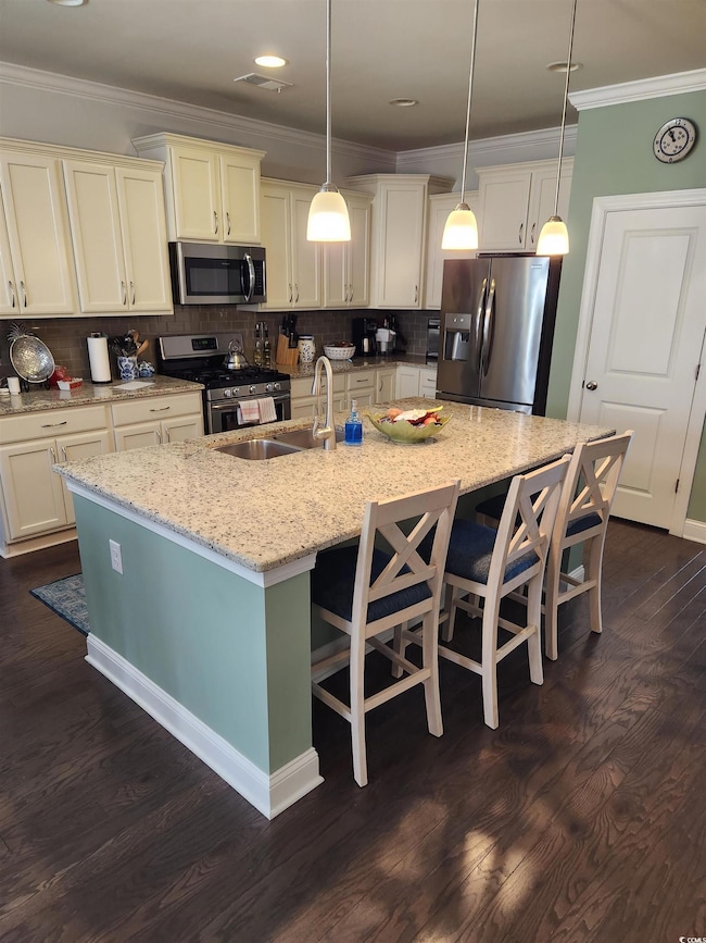 Kitchen featuring crown molding, stainless steel appliances, a breakfast bar area, a spacious island, and decorative light fixtures