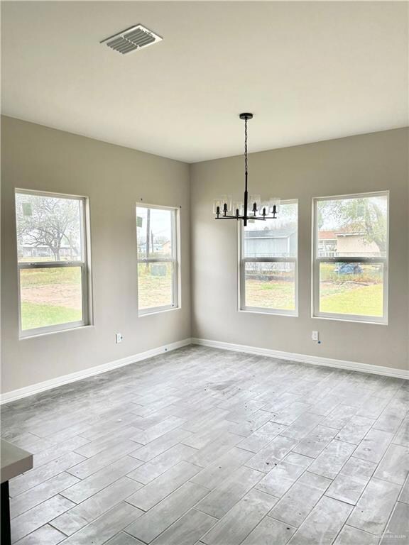 Empty room with a notable chandelier, plenty of natural light, and light wood-type flooring