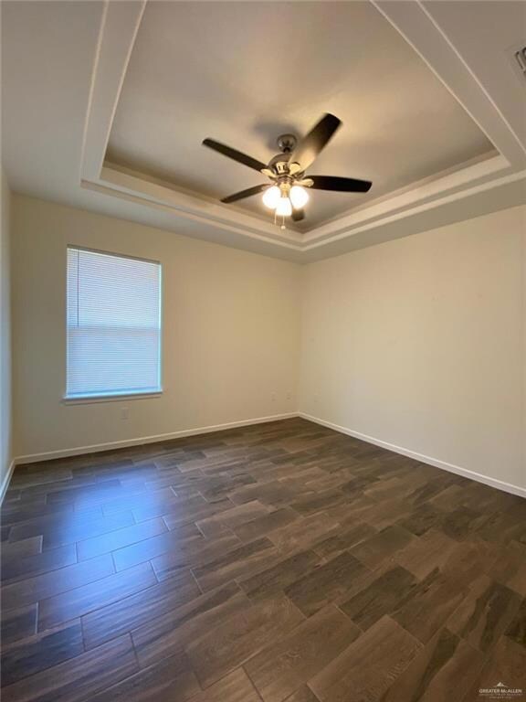 Empty room featuring a raised ceiling, dark wood-type flooring, and ceiling fan