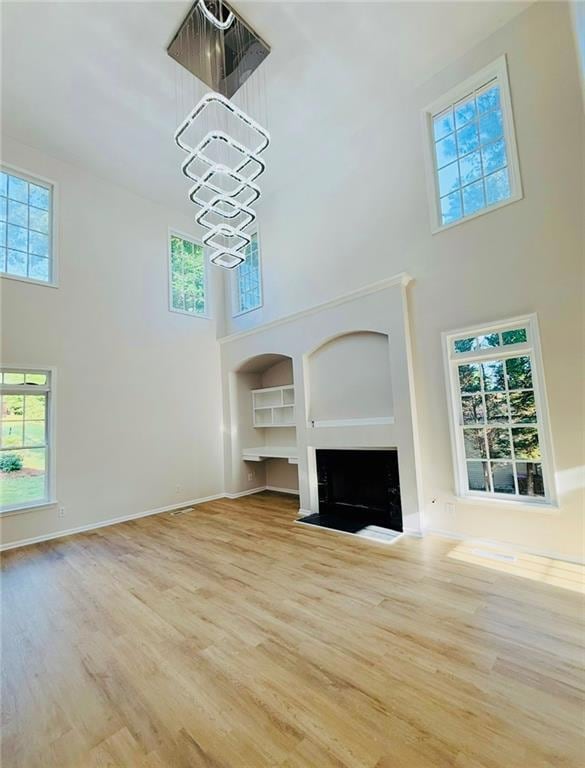 Unfurnished living room featuring a towering ceiling, a chandelier, wood finished floors, a fireplace with flush hearth, and built in features