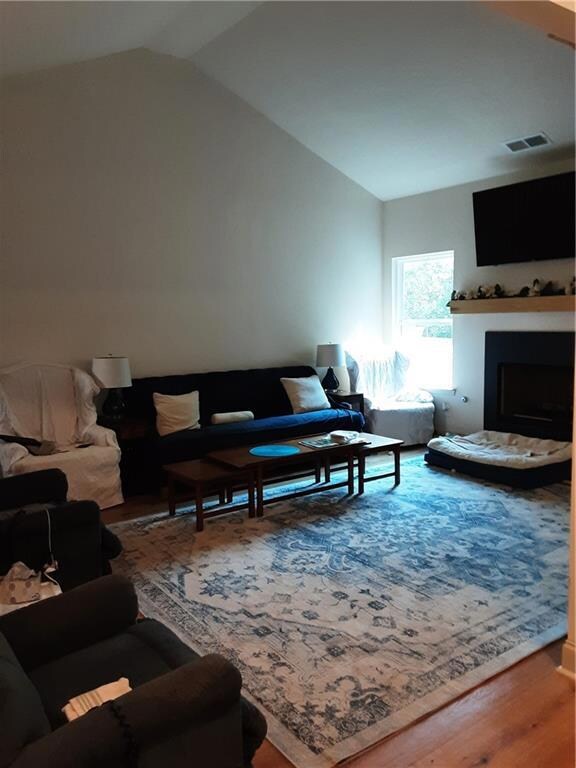 Living room featuring wood finished floors, a fireplace, and vaulted ceiling