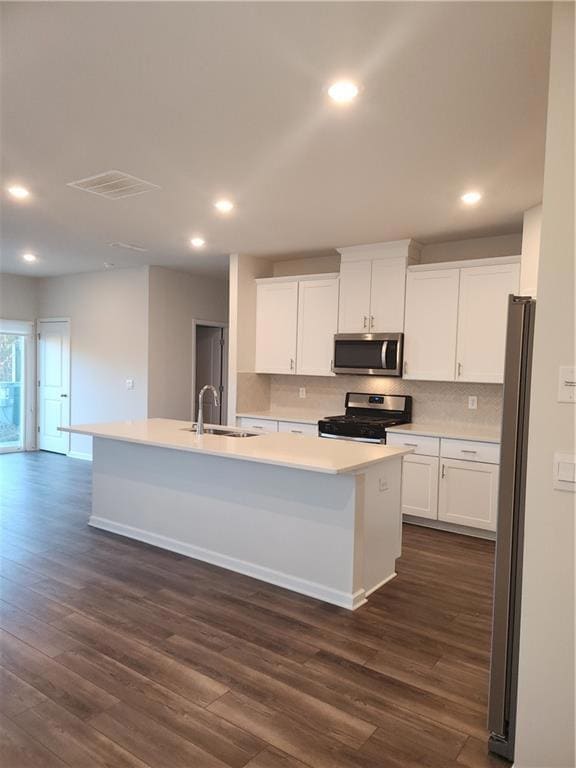 Kitchen featuring backsplash, white cabinetry, an island with sink, stainless steel stove, and recessed lighting