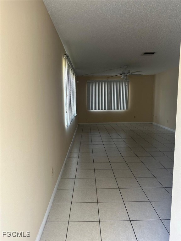 Unfurnished room with light tile patterned floors, lofted ceiling, a textured ceiling, and ceiling fan