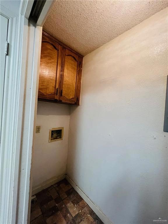 Clothes washing area with cabinets, hookup for a washing machine, and a textured ceiling