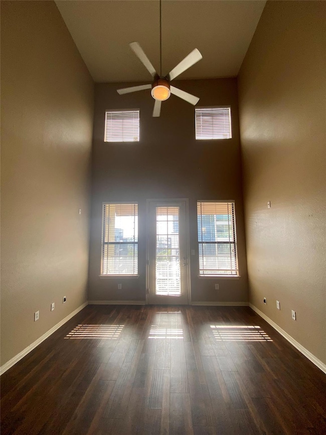 Spare room featuring a towering ceiling, dark wood-type flooring, and a ceiling fan