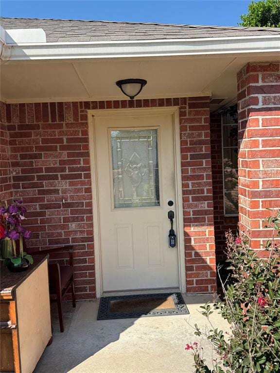 Property entrance featuring a shingled roof and brick siding