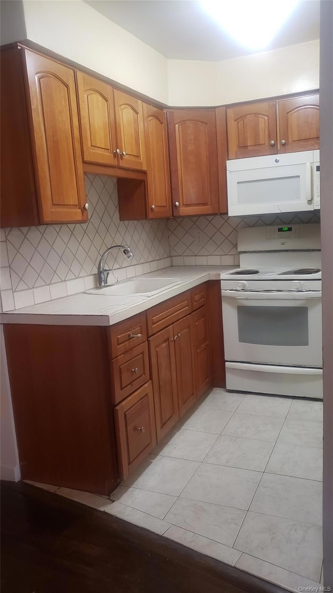 Kitchen with white appliances, brown cabinetry, light countertops, and tasteful backsplash
