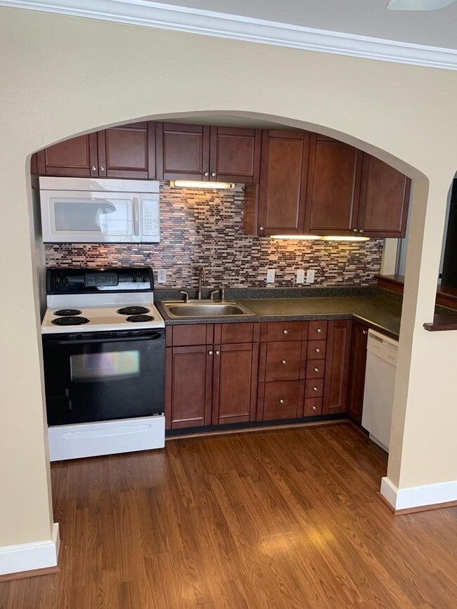 Kitchen with crown molding, white appliances, decorative backsplash, arched walkways, and dark countertops