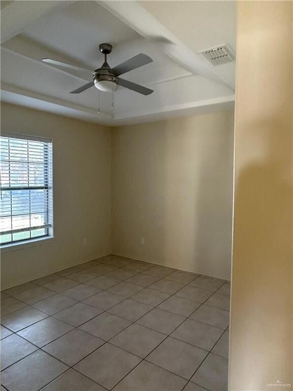 Tiled empty room featuring a tray ceiling and ceiling fan