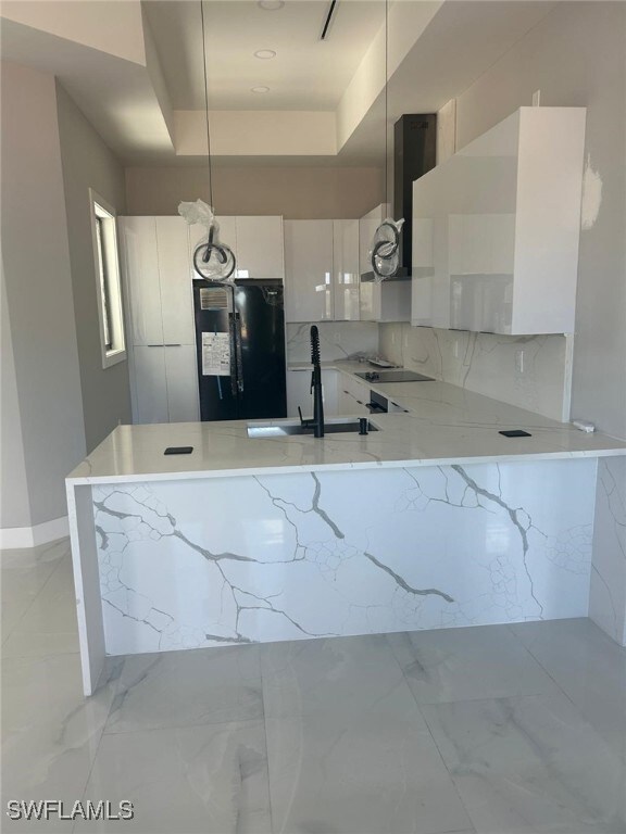 Kitchen featuring a peninsula, light stone countertops, backsplash, modern cabinets, and white cabinets