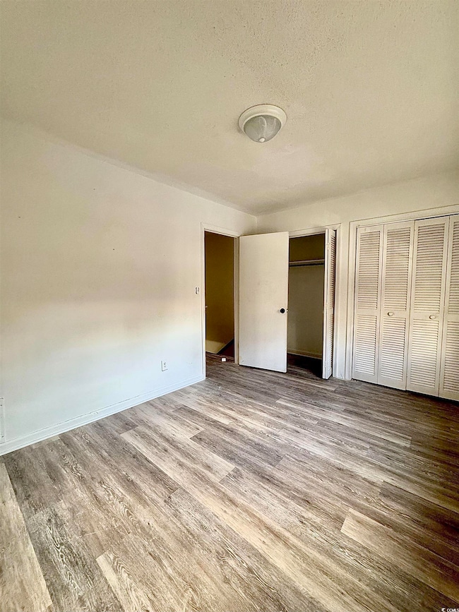 Unfurnished bedroom with multiple closets, wood finished floors, and a textured ceiling