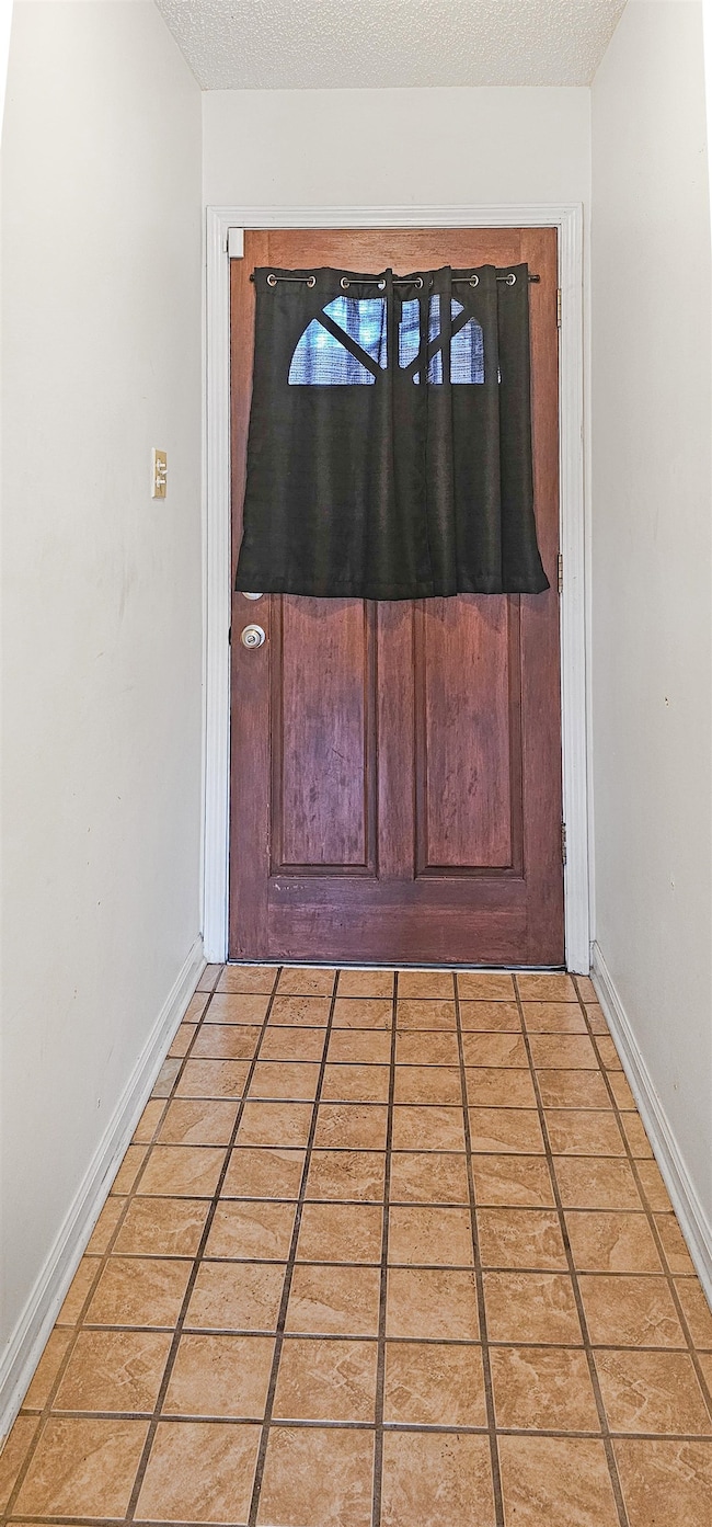 Doorway featuring baseboards, a textured ceiling, and light tile patterned floors