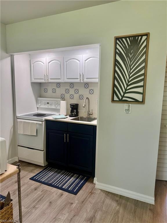 Kitchen with white electric range, light wood-style floors, white cabinets, and backsplash