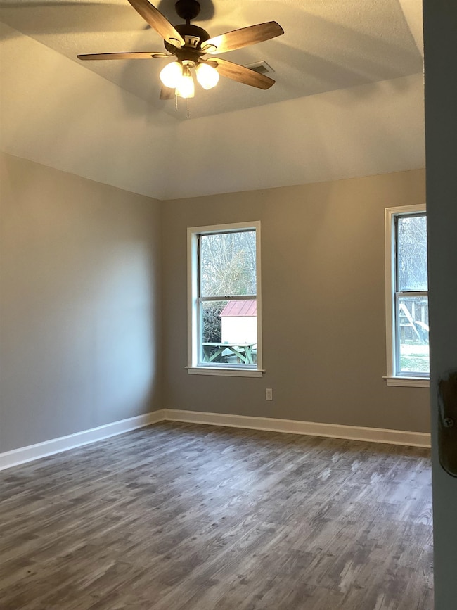 Spare room featuring dark wood-style flooring, plenty of natural light, ceiling fan, and lofted ceiling