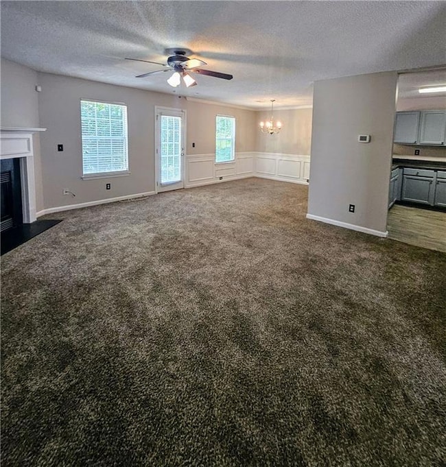 Unfurnished living room with carpet floors, a chandelier, a textured ceiling, a ceiling fan, and a high end fireplace