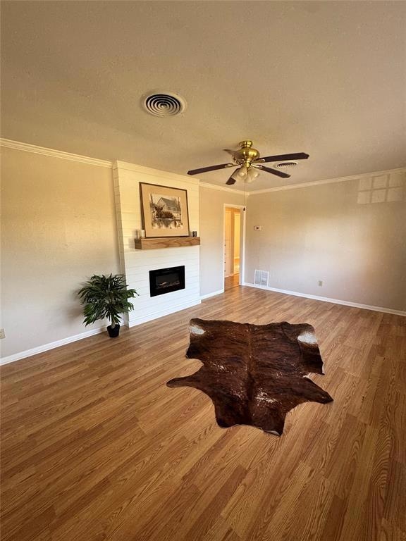 Living room featuring light wood finished floors, a glass covered fireplace, ornamental molding, ceiling fan, and a textured ceiling