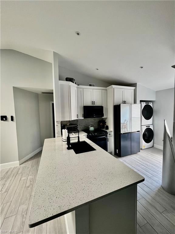 Kitchen with stacked washing machine and dryer, light Spanish tile flooring, electric range, decorative backsplash, and white cabinetry