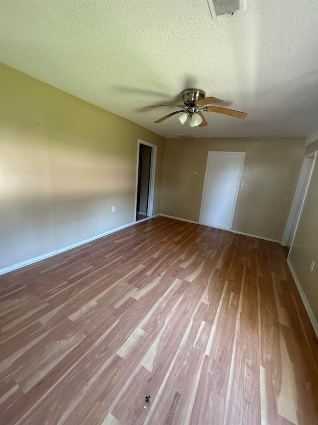 Spare room with wood finished floors, a ceiling fan, a textured ceiling, and baseboards