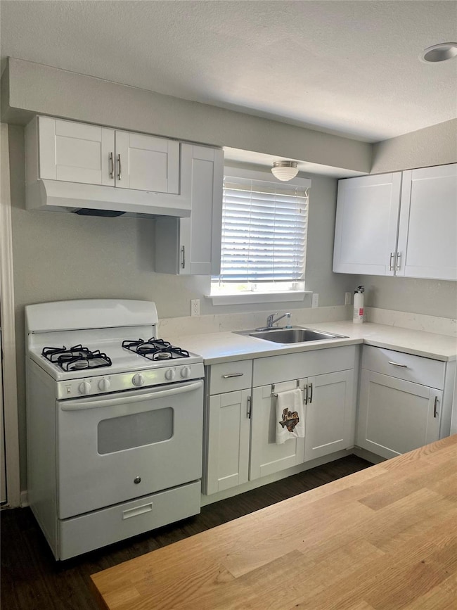 Kitchen featuring white gas range, white cabinetry, dark wood finished floors, under cabinet range hood, and butcher block countertops