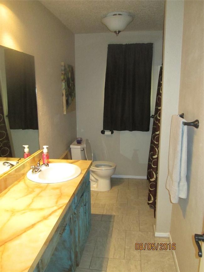 Full bath featuring a textured ceiling, vanity, a shower with shower curtain, and light tile patterned floors
