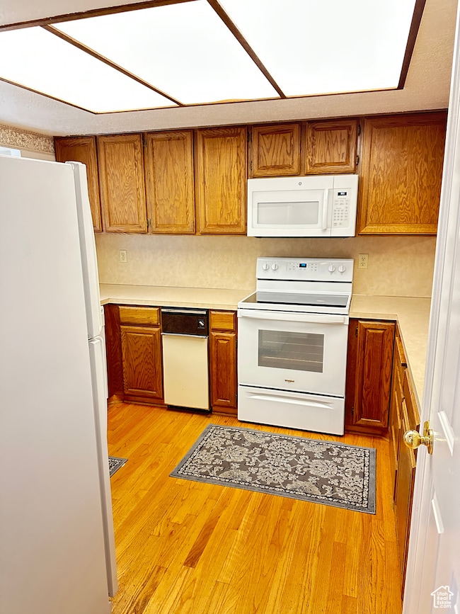 Kitchen with white appliances, light countertops, brown cabinets, and light wood-style flooring