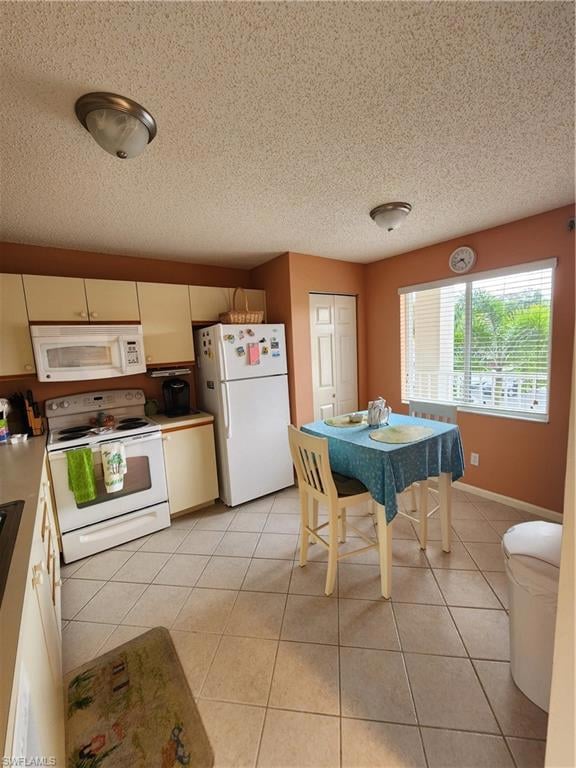 Kitchen featuring range, freestanding refrigerator, a textured ceiling, light tile patterned floors, and light countertops