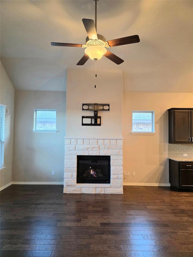 Unfurnished living room with dark wood finished floors, lofted ceiling, a fireplace, and ceiling fan