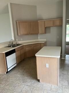 Kitchen featuring white dishwasher, sink, light tile floors, and a kitchen island