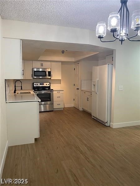 Kitchen with light countertops, appliances with stainless steel finishes, hanging light fixtures, white cabinetry, and dark wood finished floors