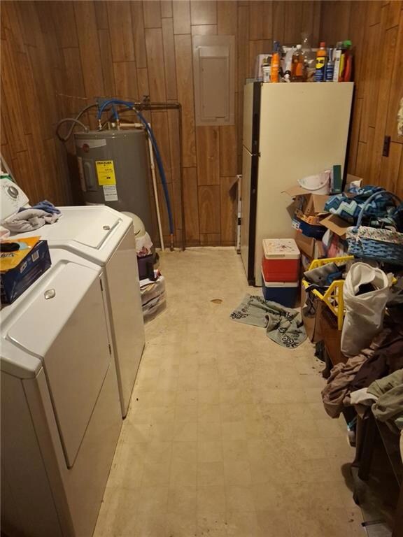 Laundry area featuring wood walls, light floors, water heater, separate washer and dryer, and electric panel
