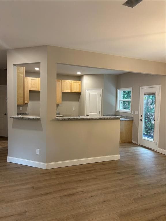 Kitchen featuring wood finished floors, light brown cabinets, a peninsula, recessed lighting, and stone countertops