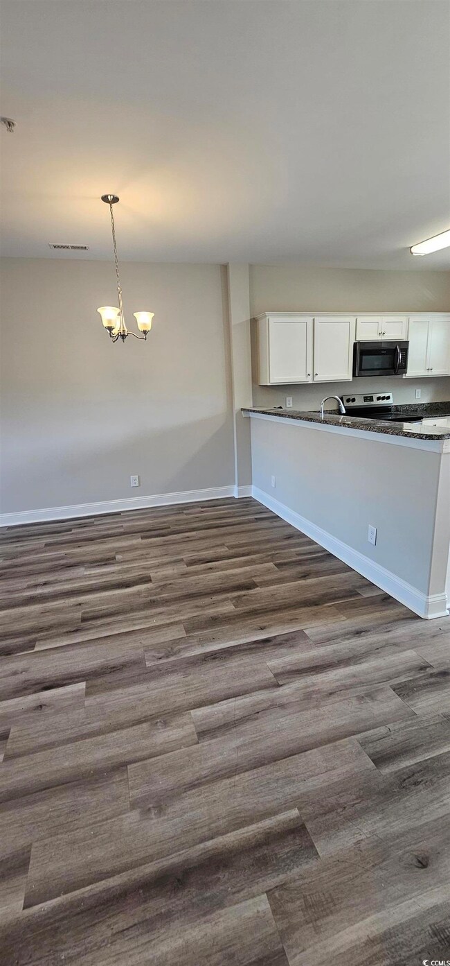 Kitchen with black microwave, dark wood-style floors, and white cabinets