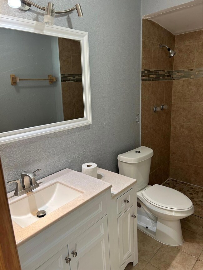 Bathroom with tile patterned flooring, vanity, toilet, and a tile shower