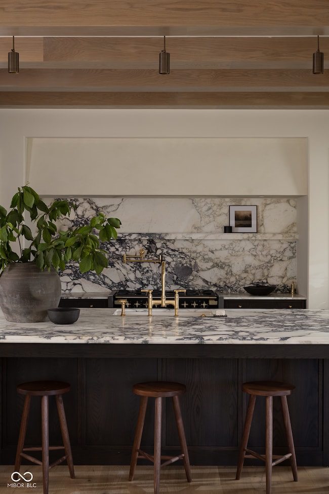 Kitchen featuring custom hood, natural marble counters, and backsplash