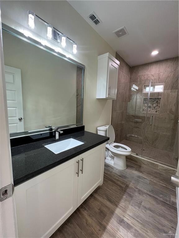 Bathroom featuring a shower with door, vanity with extensive cabinet space, hardwood / wood-style floors, and toilet